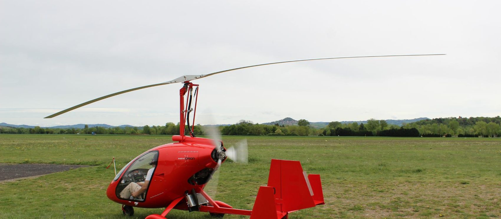 A red gyroplane parked on a grass airfield