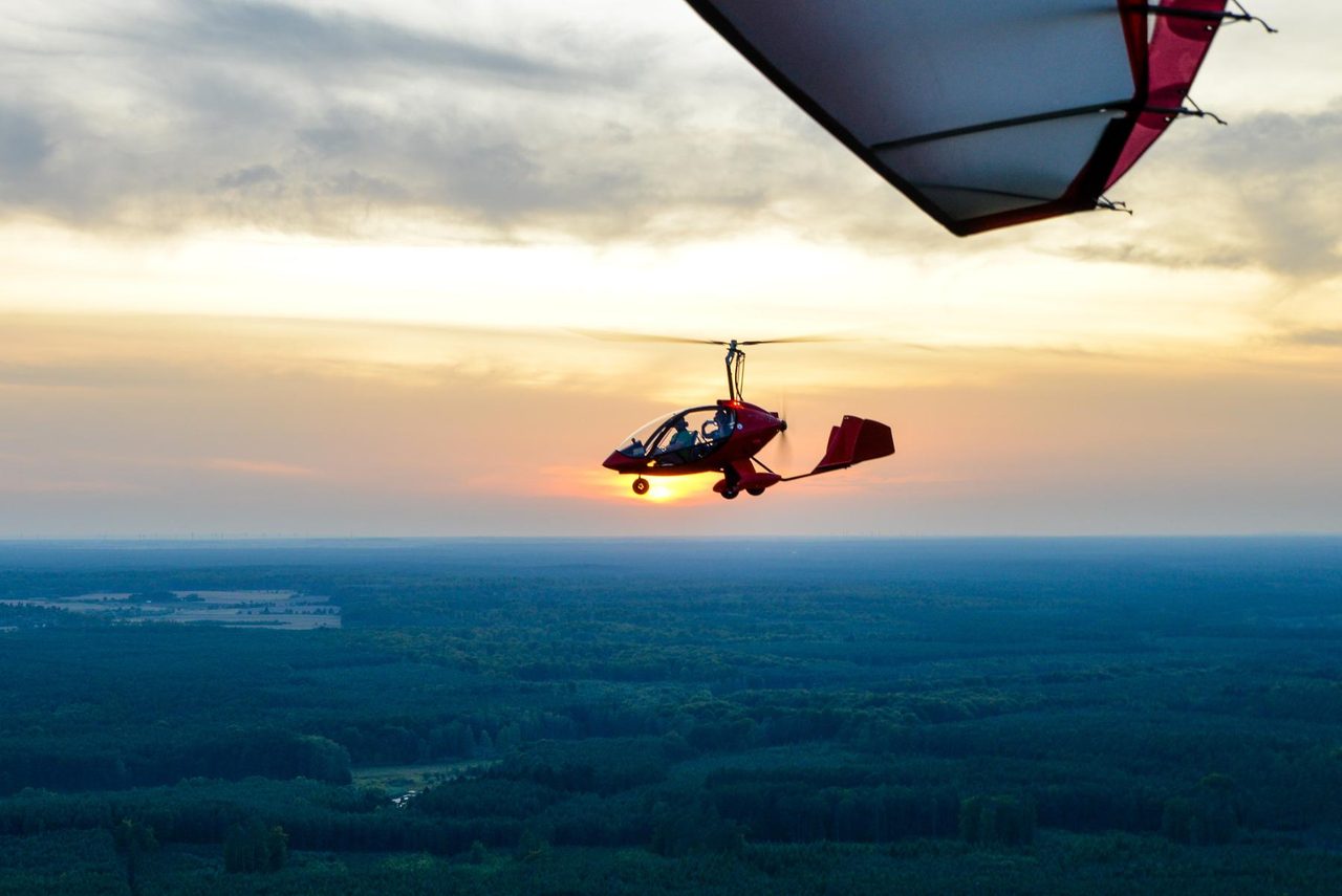 A small aircraft in flight above forest at sunset.