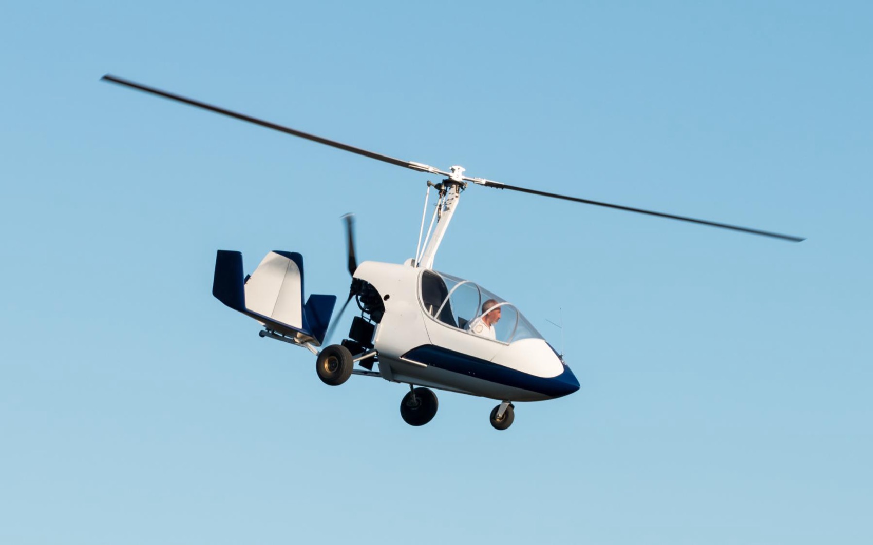 A white gyroplane in flight against blue sky