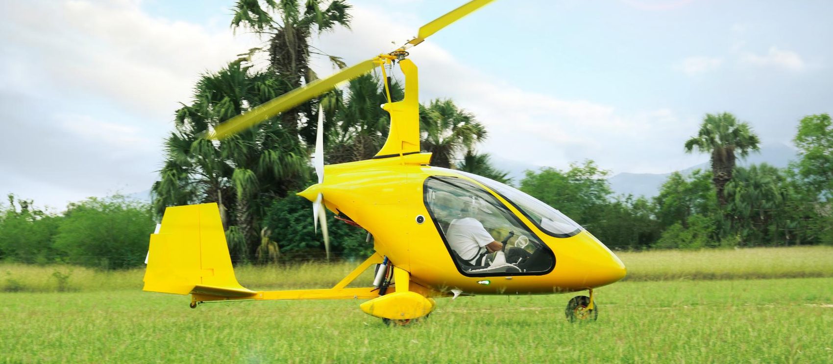 A yellow gyroplane on grass with the rotor turning